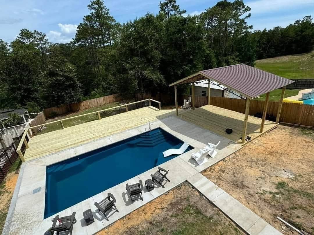 Aerial view of a residential pool with deck, lounge chairs, and poolhouse surrounded by green landscaping