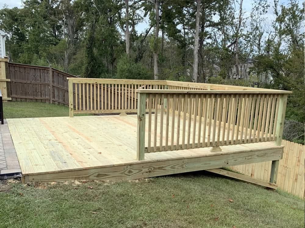 Newly constructed wooden deck with railings and steps in a Northwest Florida backyard surrounded by tall trees