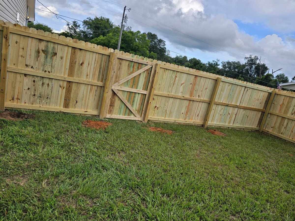 New wooden fence panels installed along a green lawn with trees and cloudy sky in the background